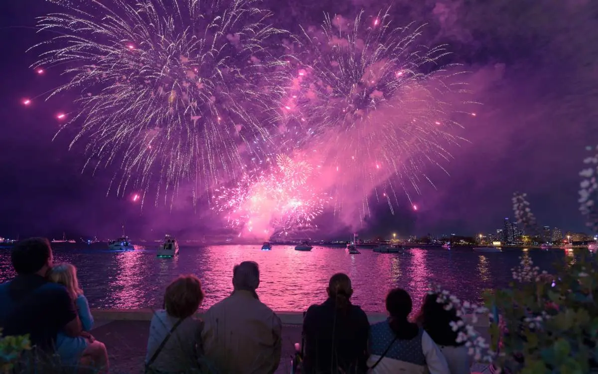 People sitting on the Lake Michigan shore watching fireworks over Chicago