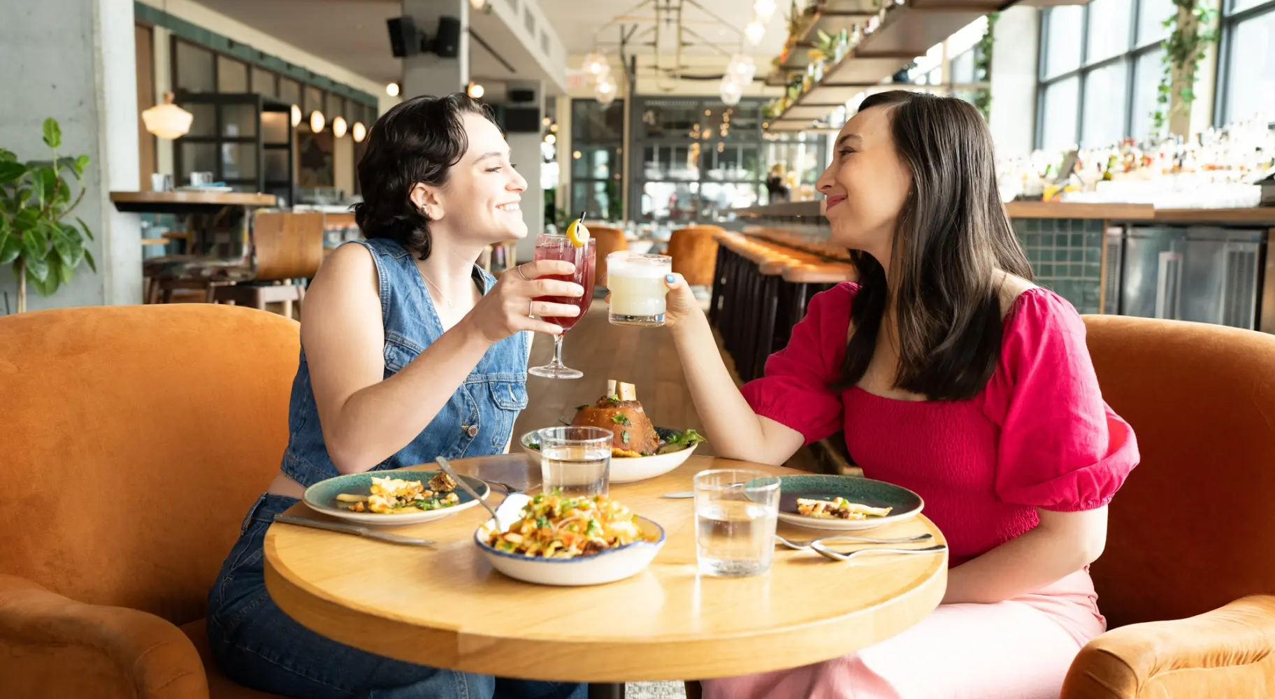 Two people clinking glasses at a small table at Cabra, a rooftop bar