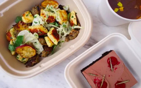 Birds eye view of a cherry cake and savory meal in takeaway boxes