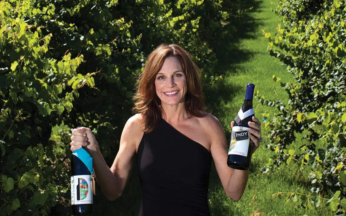 A woman in a vineyard holding up two bottles of wine