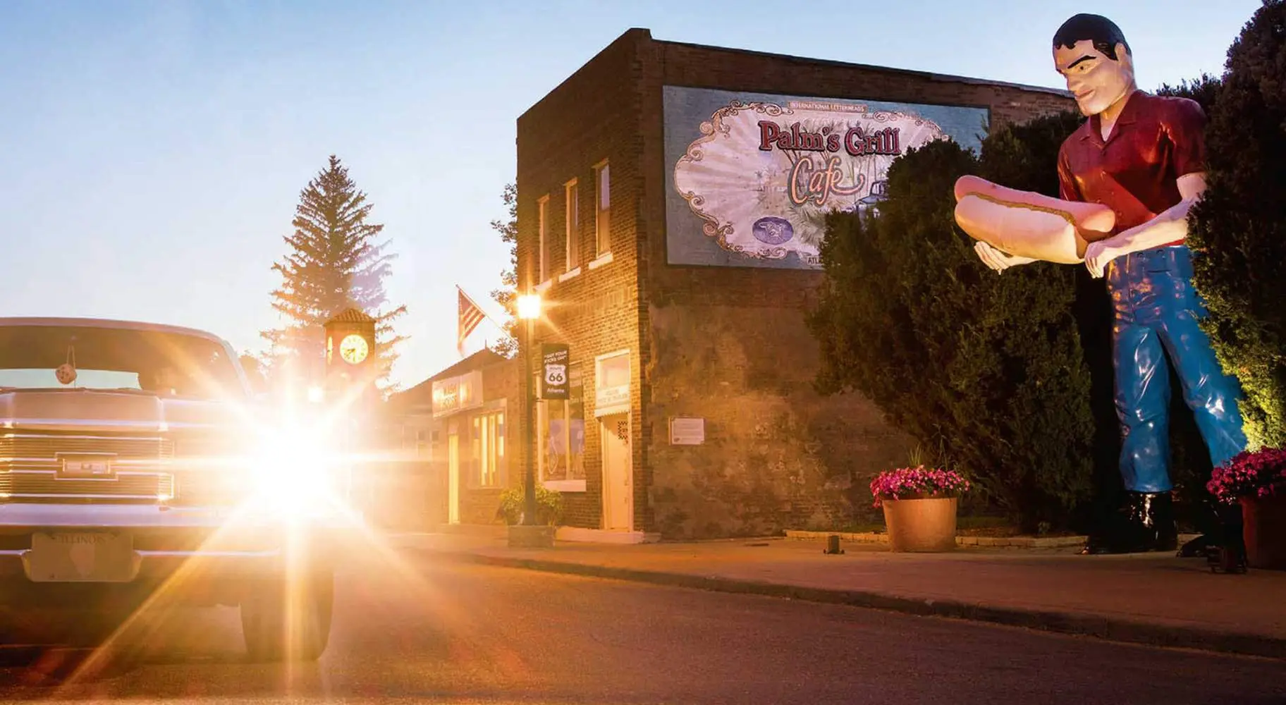 Sunsetting behind a car with a giant statue of a man holding a hotdog