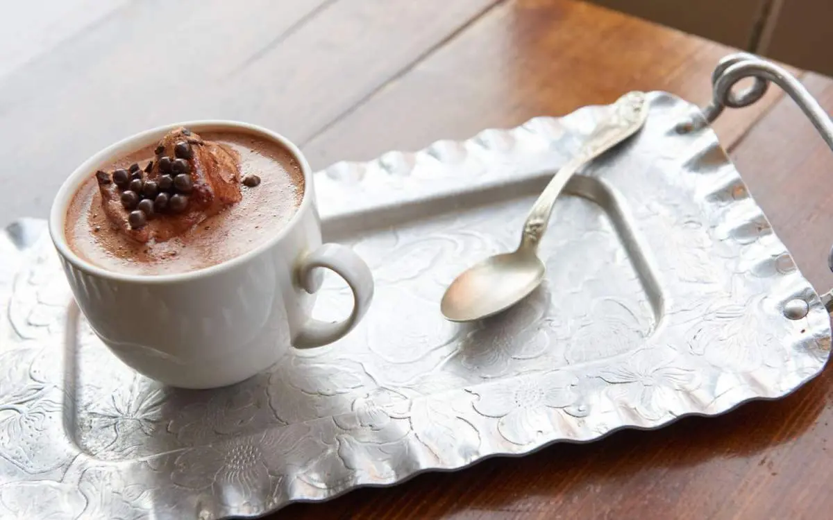 A mug of hot chocolate and teaspoon sitting on top of a serving tray