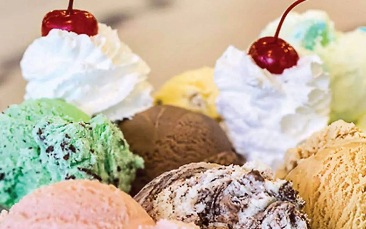 A bowl filled with different flavours of ice cream and topped with cherries