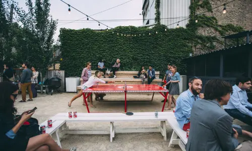 Patrons drinking beers and playing table tennis in the outdoors