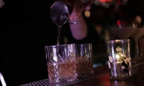 A bartender pours drinks into glasses.