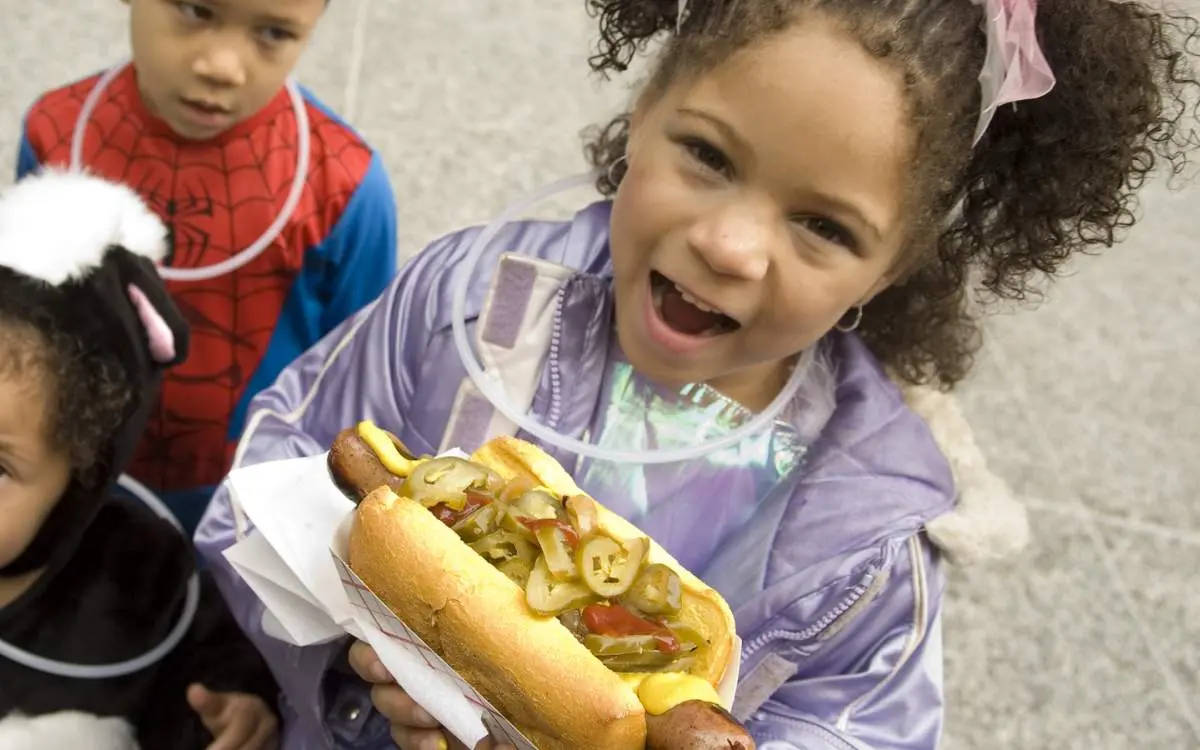 Three kids one holding a Chicago style hot dog