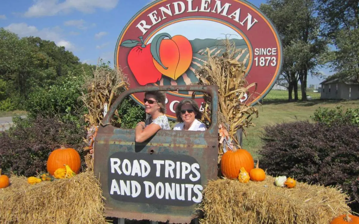Two people posing in behind a pumpkin haystack and metal truck door at an orchard