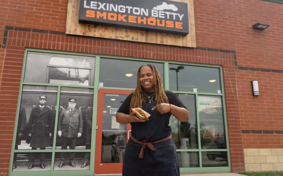 A woman holding a hotdog in front of the Lexington Betty Smokehouse.