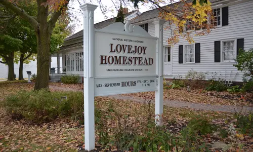 A white sign for the lovejoy homestead with autumn leaves around