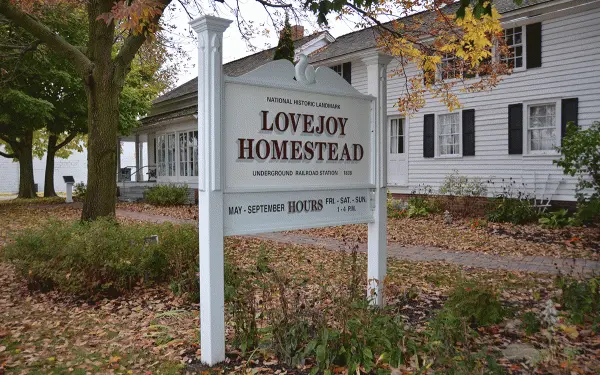 A white sign for the lovejoy homestead with autumn leaves around