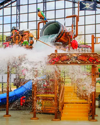 A dump bucket splashes water over a pirate-themed play tower at an indoor water park