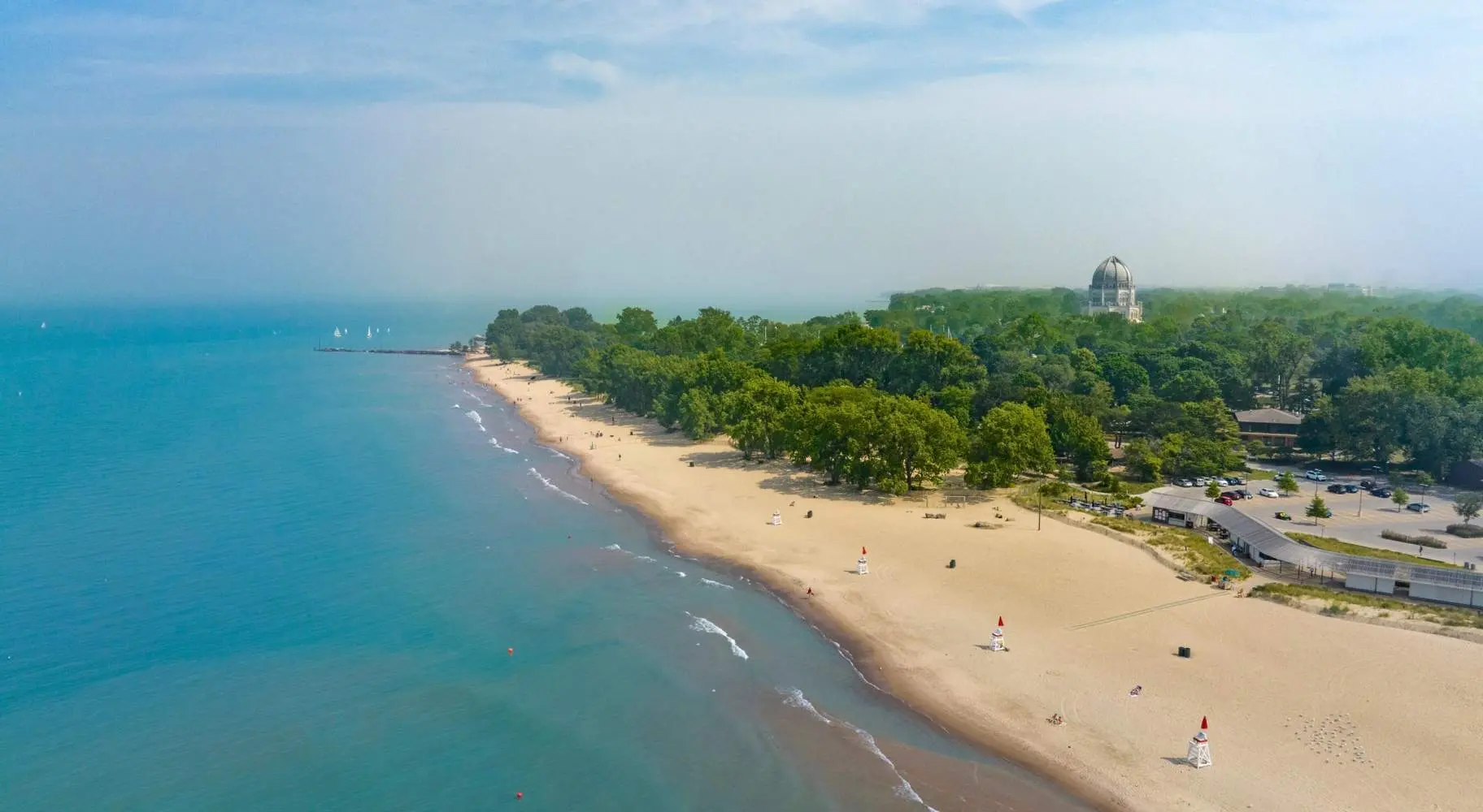 An aerial shot of a beach coastline, with green trees in the background