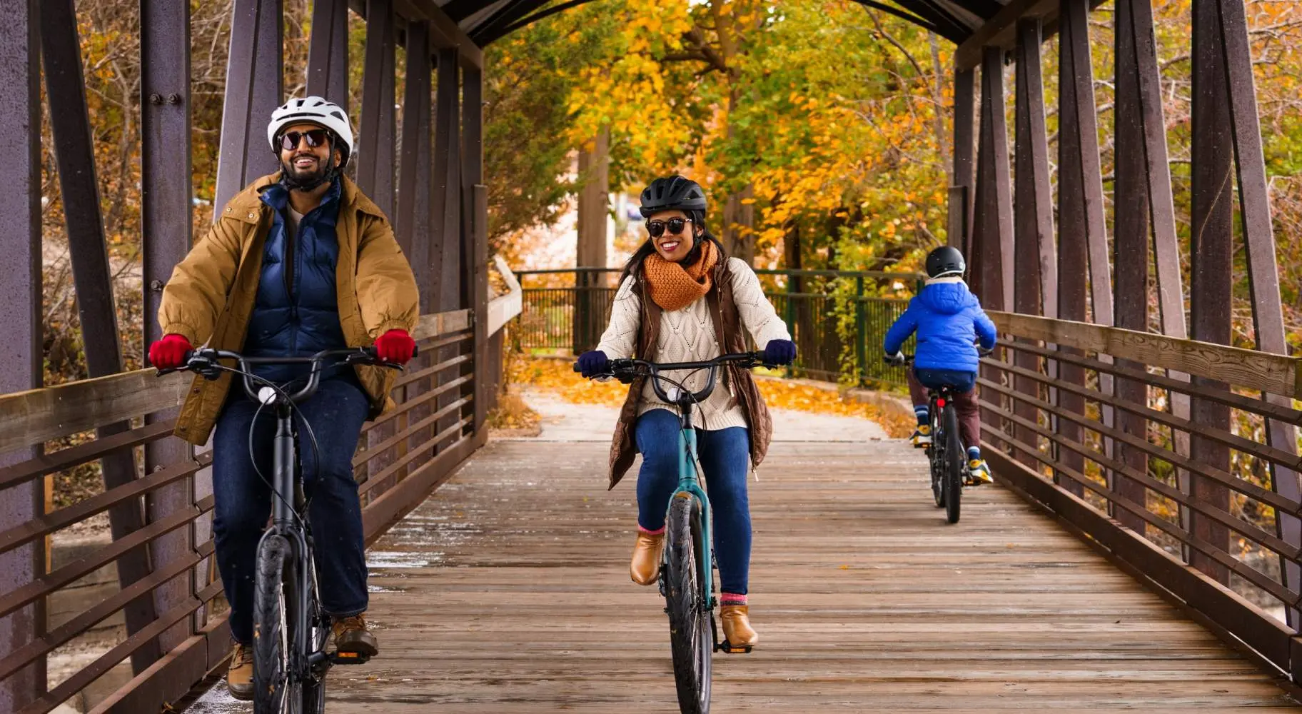 A couple riding bikes on an old wooden covered bridge, with fall foliage behind them