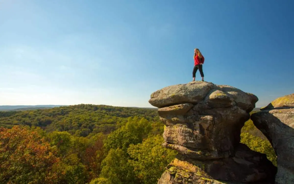 Hiker on top of a large rock over looking the forest.