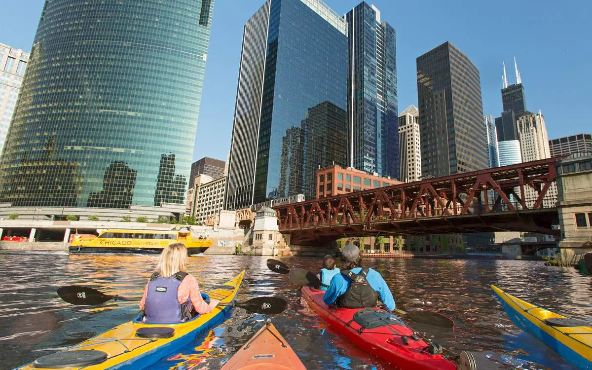 A group of people in kayaks on the Chicago River, in front of a group of high-rise buildings.