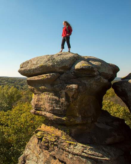 Woman standing on a large rock overlooking the forest below