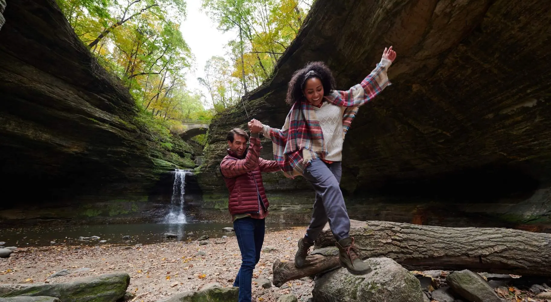 Two people climbing on rocks in front of a rock waterfall