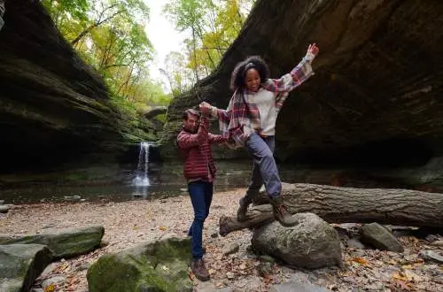 Two people climbing on rocks in front of a rock waterfall