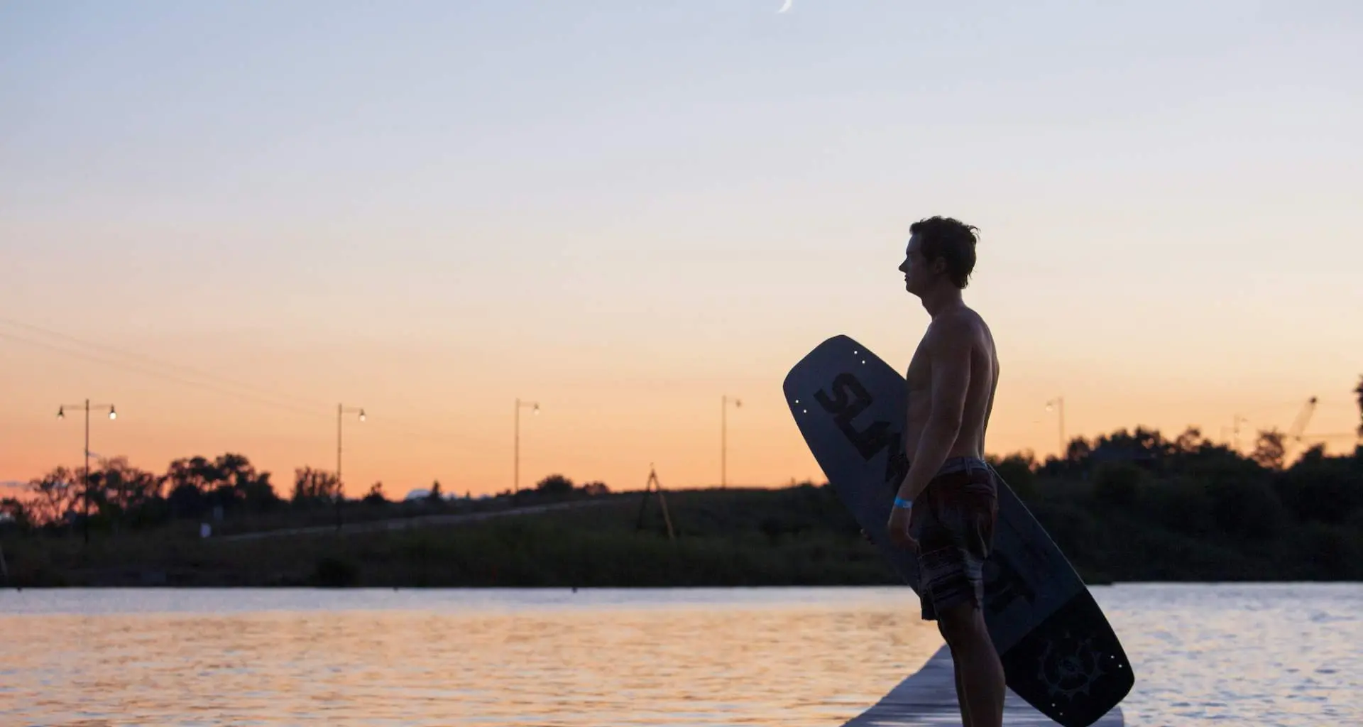 Wakeboarder stands next to Quarry Cable Park at dusk