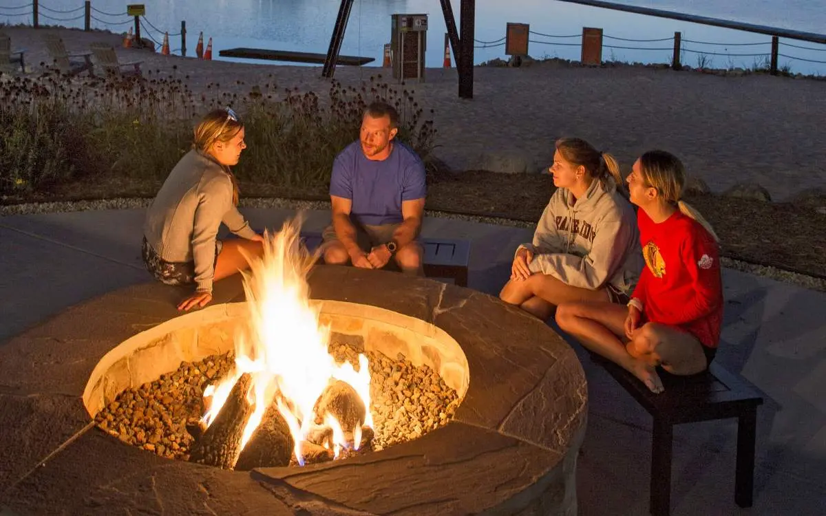 People sitting down a fire-pit with a lake behind them