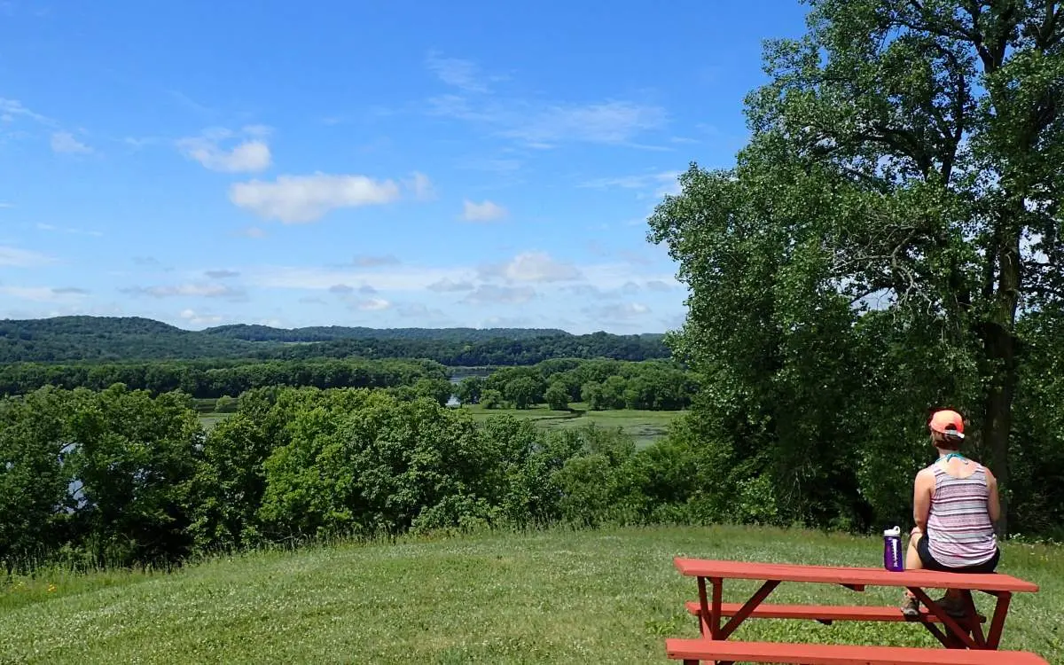 A person sitting on a picnic table looking out to land and trees