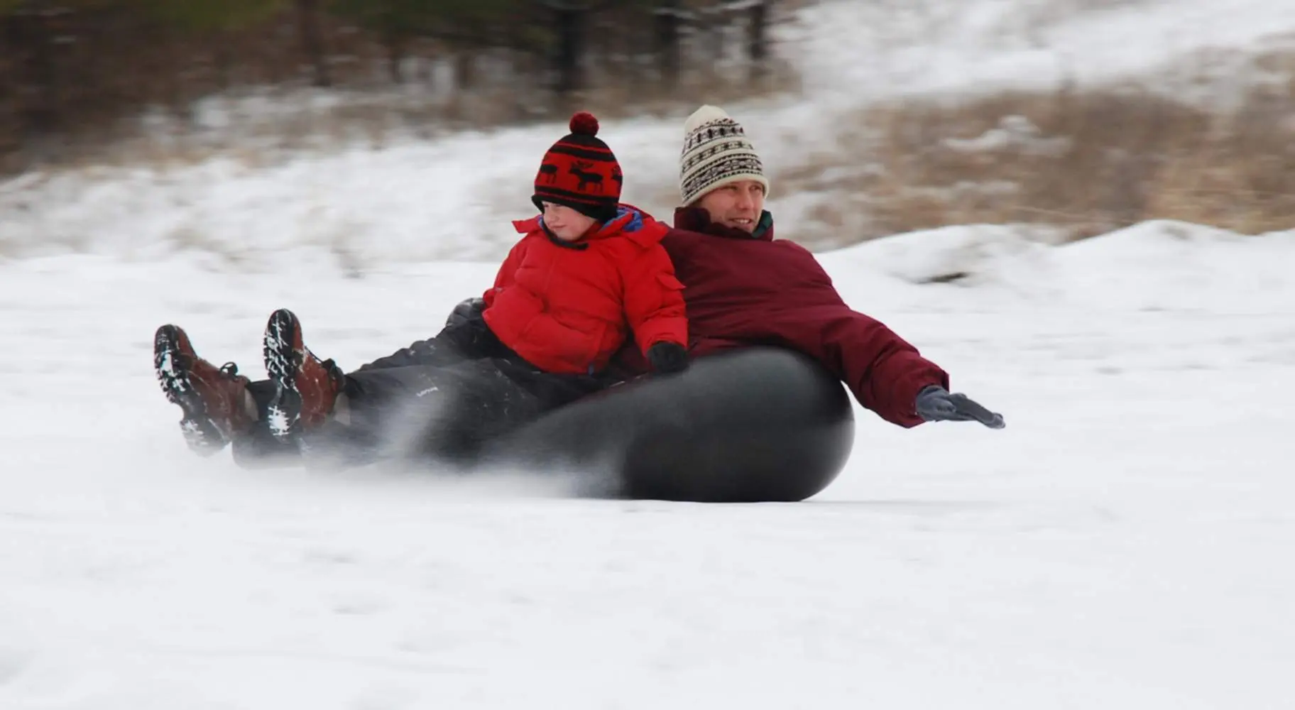 A man and a boy snowtubing on Mount Hoy