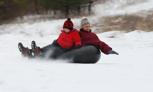 A man and a boy snowtubing on Mount Hoy