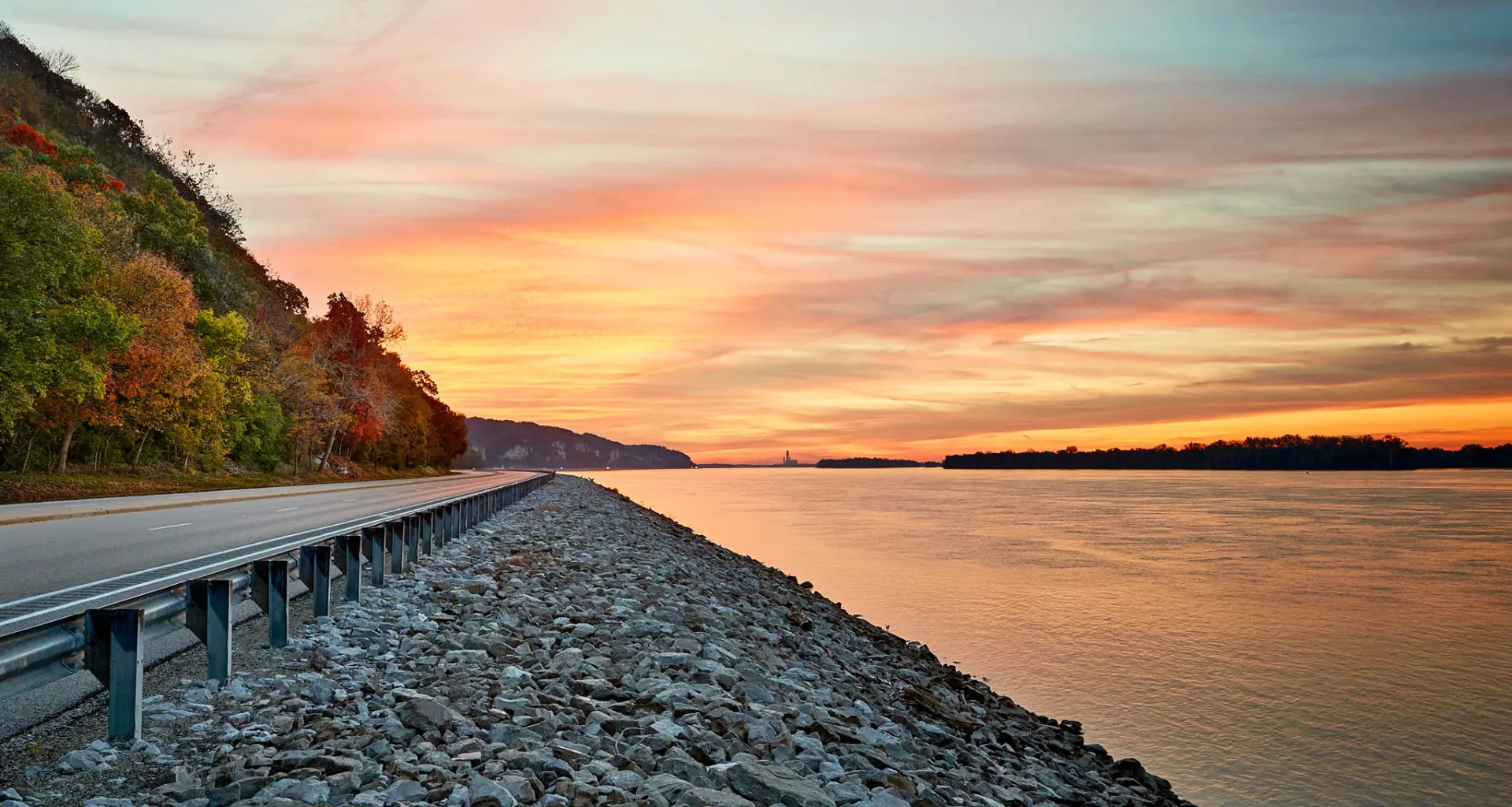 Sunset shining over water and a road beside the river