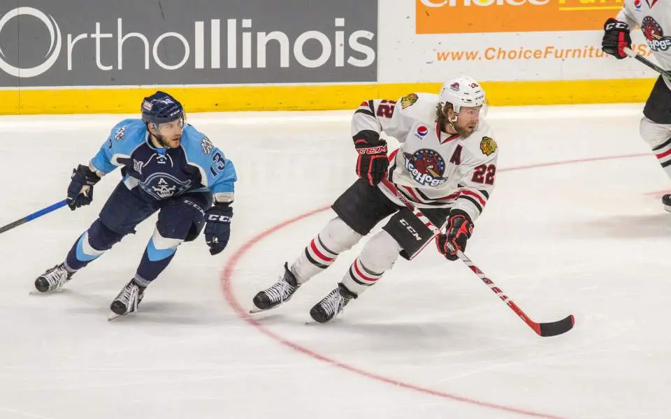 A Rockford Icehogs ice hockey player being pursued by an opposing player on the ice