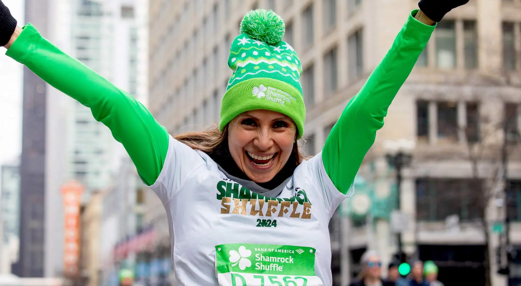 A running race participant in green with her arms raised in the air